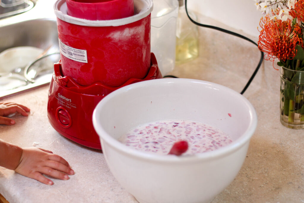 White bowl of strawberries and cream sitting on counter next to ice cream maker