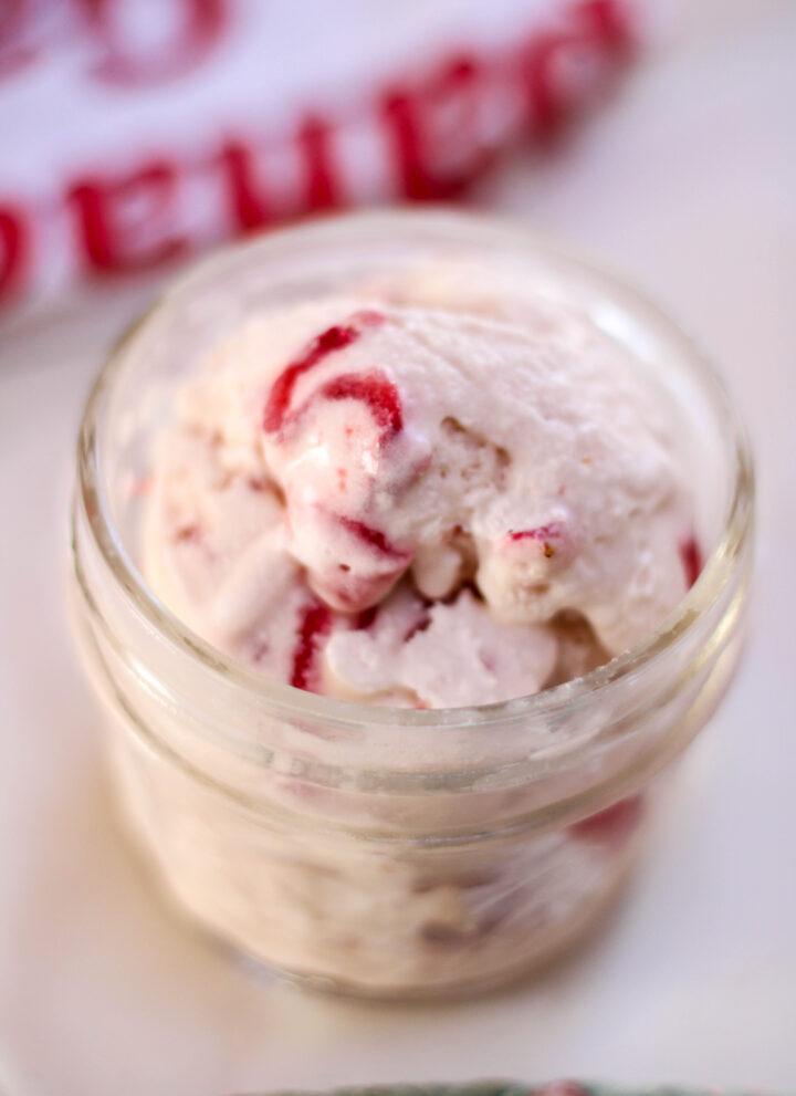 A scoop of helado de fresa in a glass jar on a white table with towels in the background