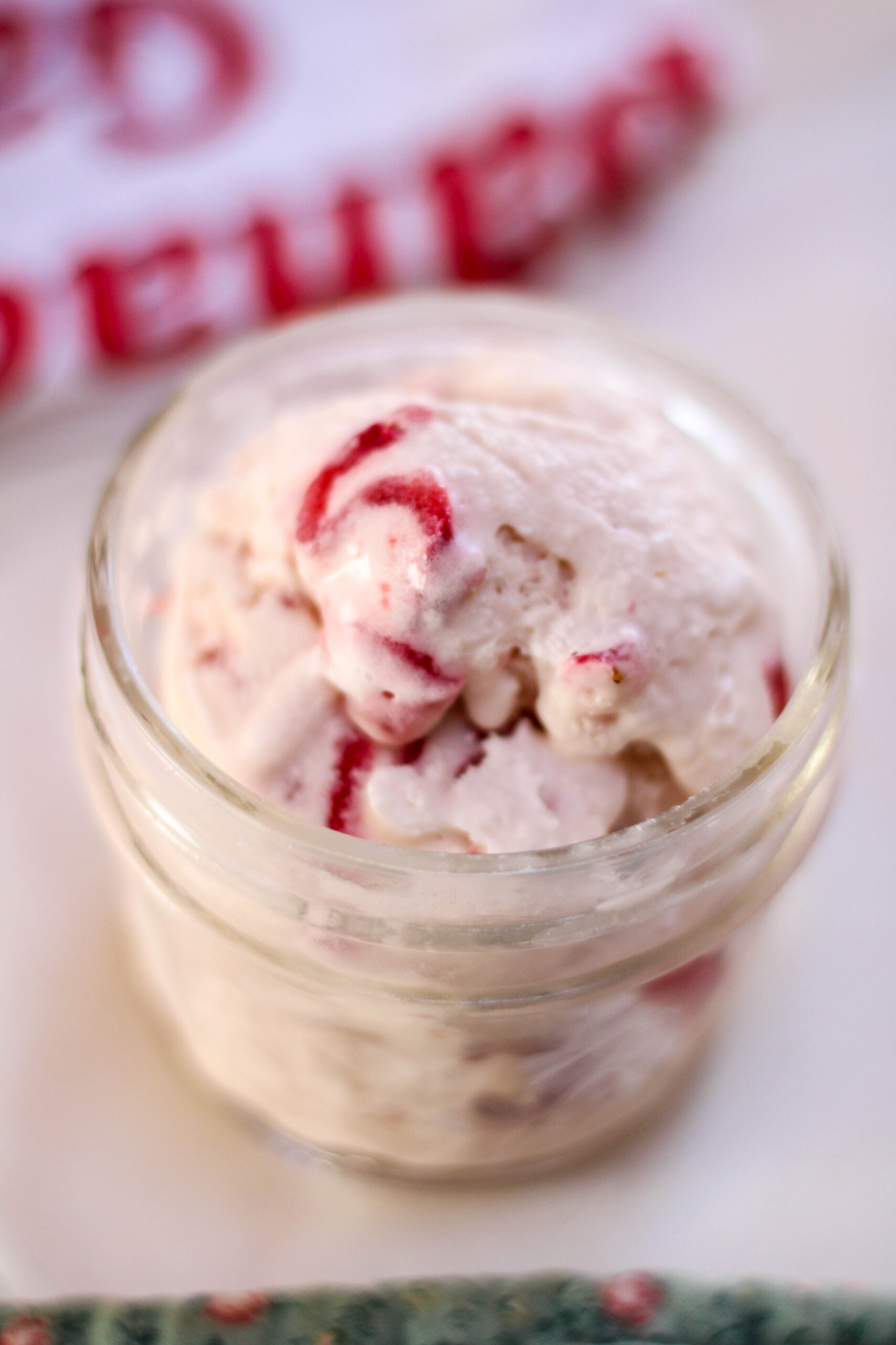A scoop of helado de fresa in a glass jar on a white table with towels in the background