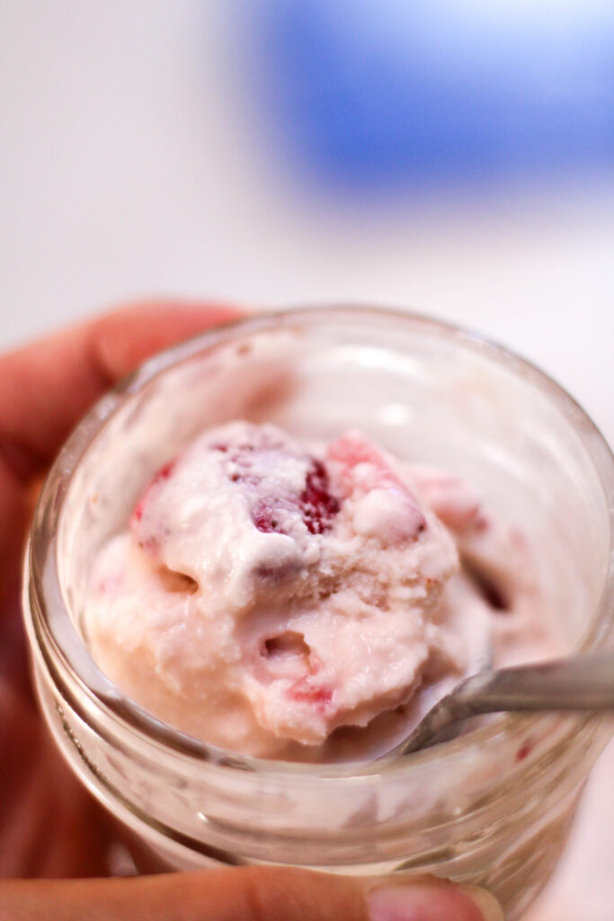 Hand holding a scoop of helado de fresa in a glass jar with white and blue background
