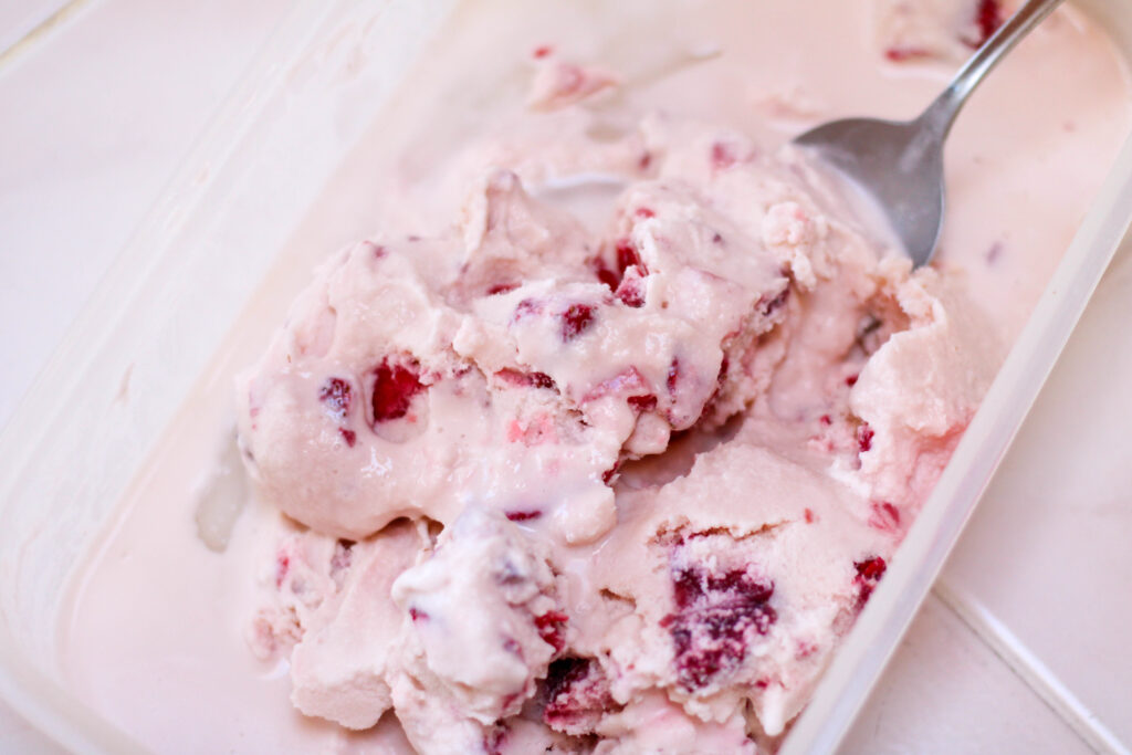 Large container of helado de fresa with spoon on a white table