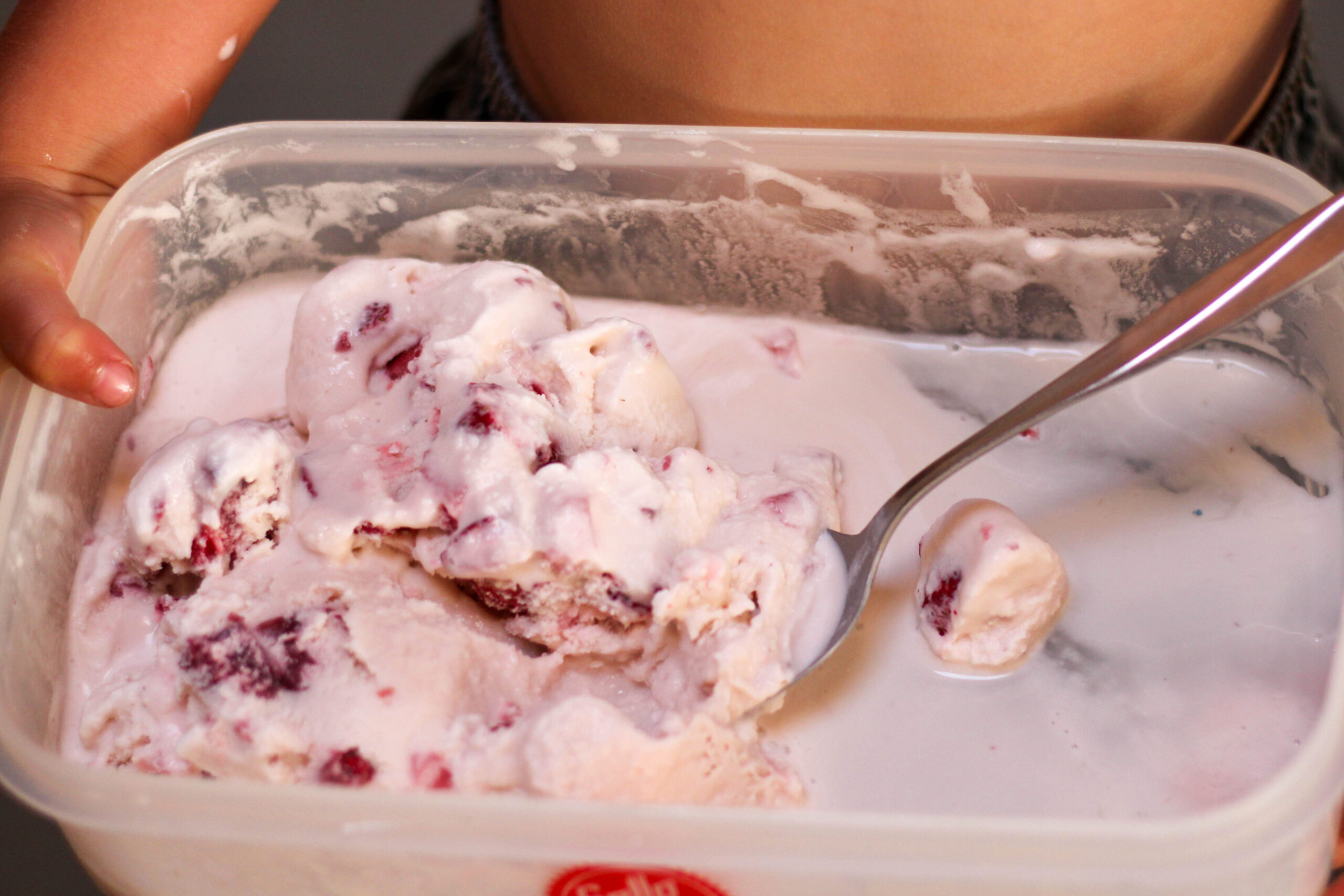 Kid holding large container of helado de fresa with a metal spoon