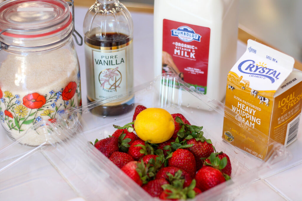 Ingredients for homemade strawberry ice cream including cream, milk, strawberries, lemon, vanilla and sugar