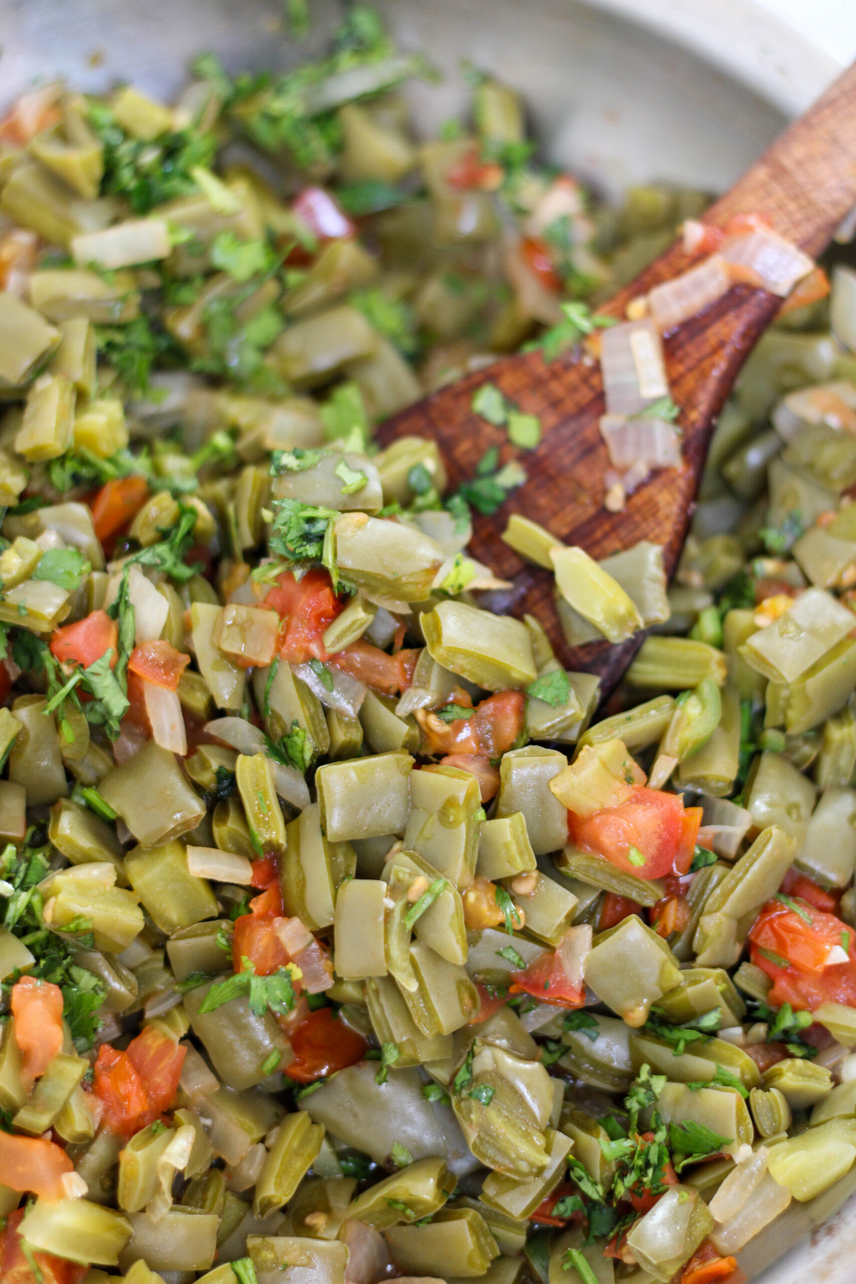 Nopales salad with tomato and onion in a pan with a wood serving spoon