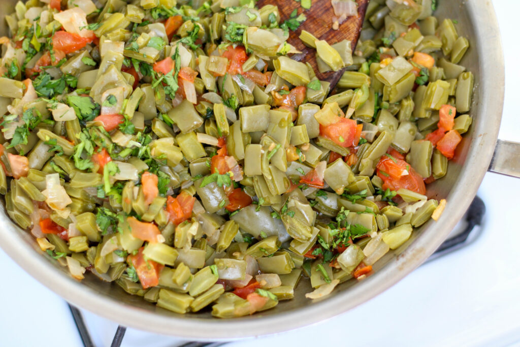 Nopalitos with tomato, onion and cilantro in a pan on a white stove