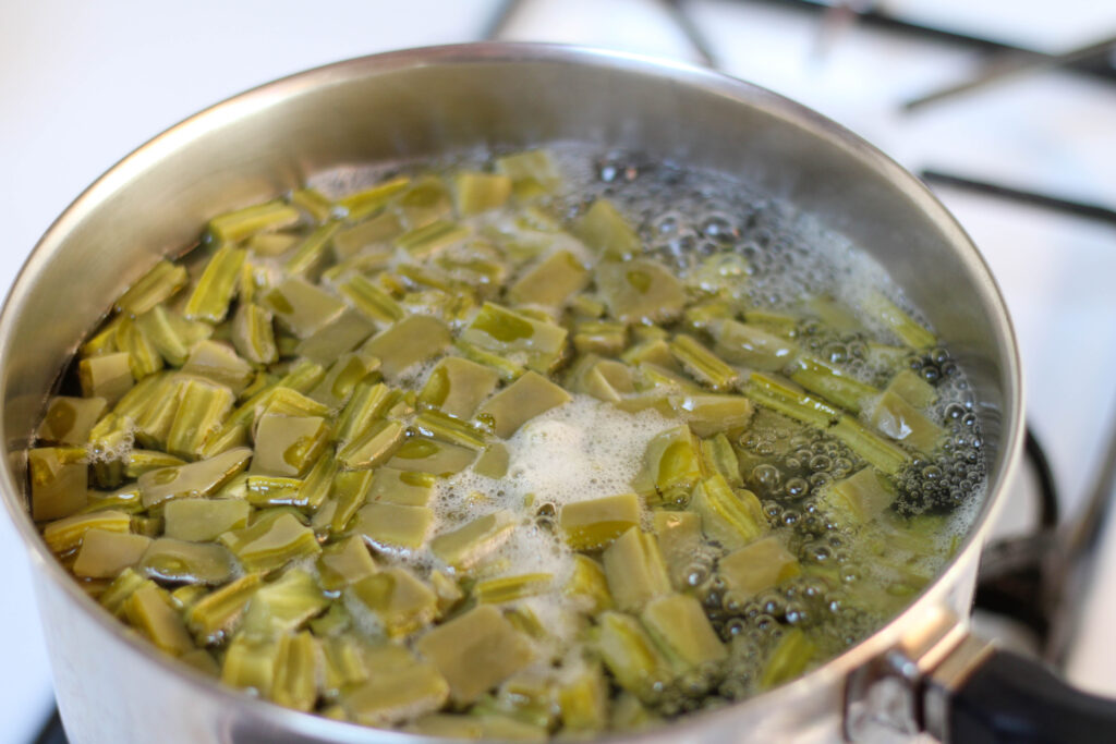 Nopales in boiling water in a saucepan on a white stove