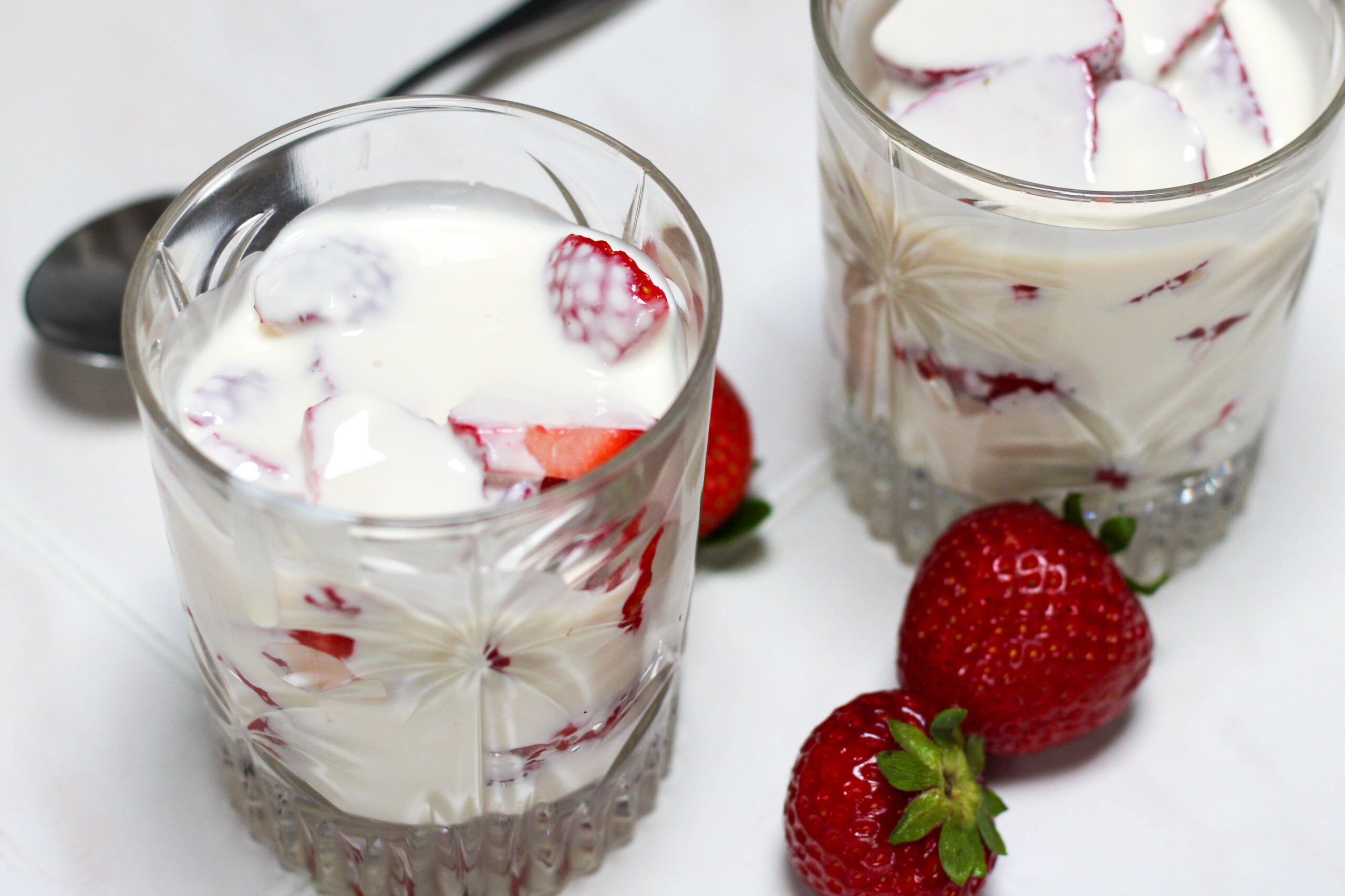Two glasses of fresas con crema on a white table with spoon and strawberries