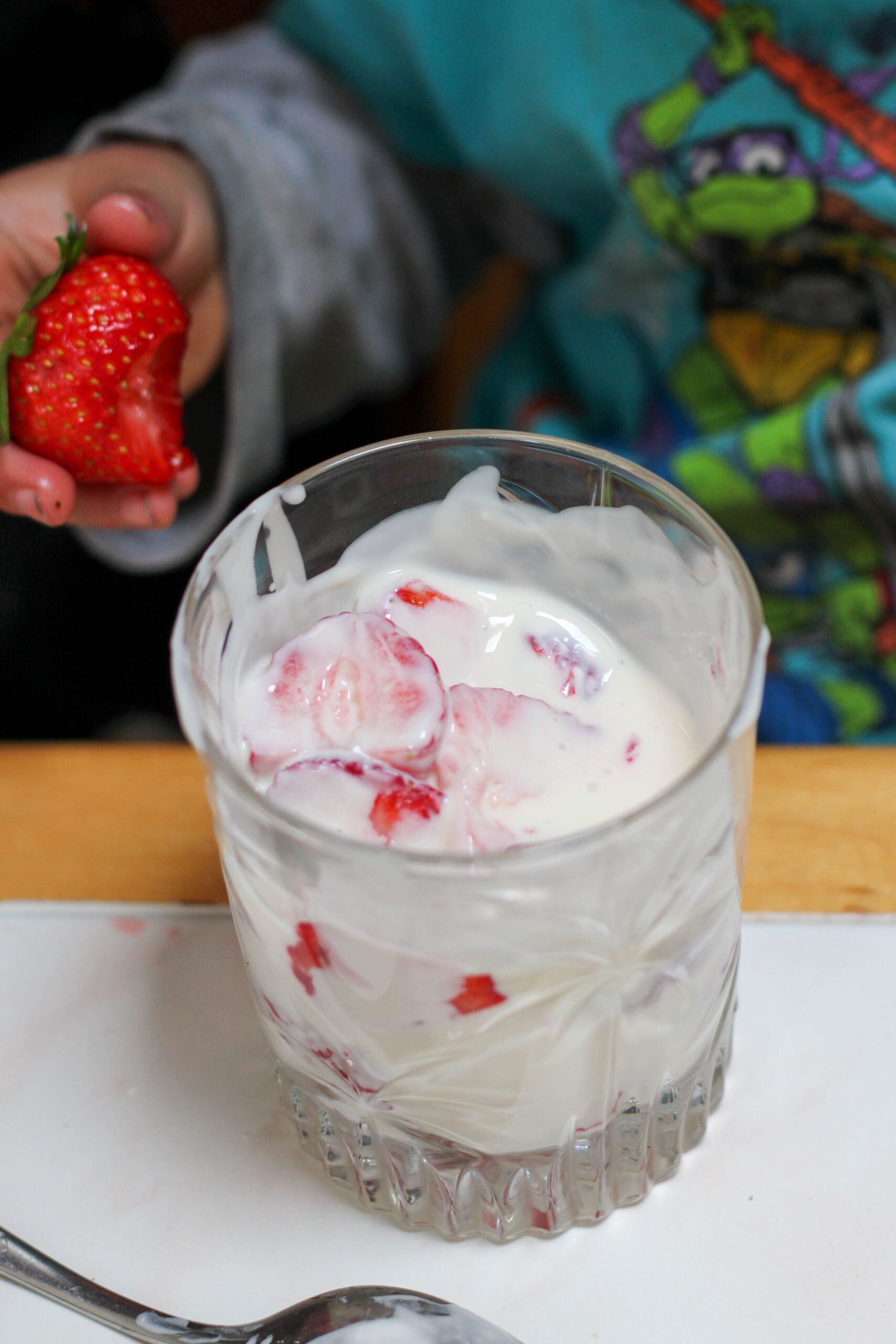 Glass of fresas con crema on a white table with boy with strawberry in hand in background