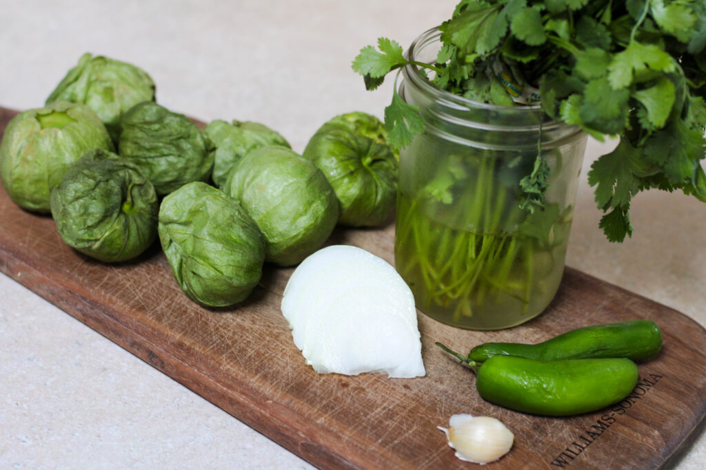 Tomatillos, onion, cilantro, serrano peppers and garlic on a wooden cutting board