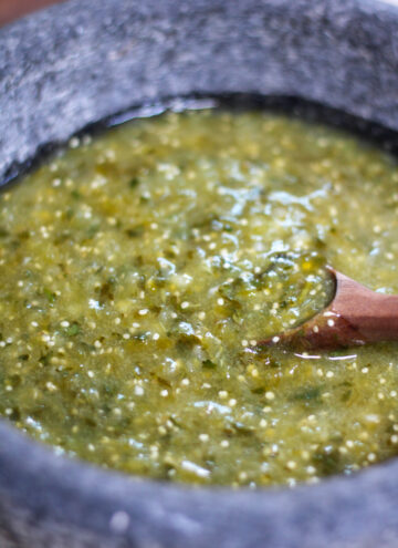 Green salsa verde in a molcajete or mortar with wooden spoon