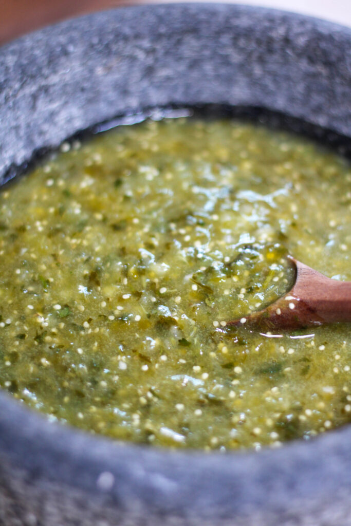 Green salsa verde in a molcajete or mortar with wooden spoon