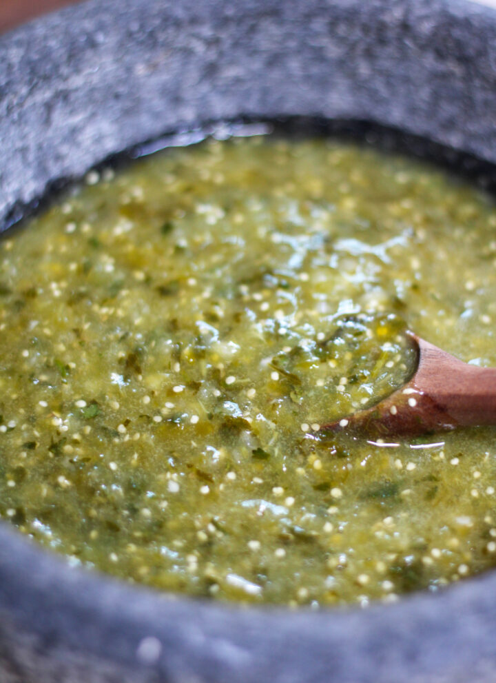 Green salsa verde in a molcajete or mortar with wooden spoon