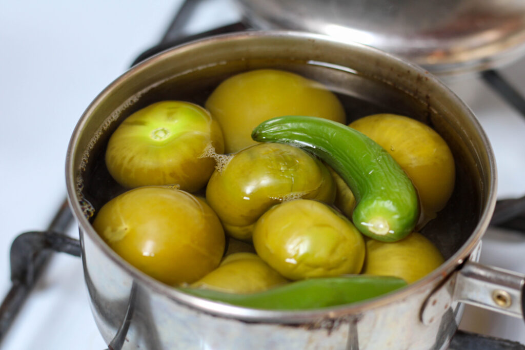 Tomatillos and serrano peppers boiling in a saucepan on a white stove