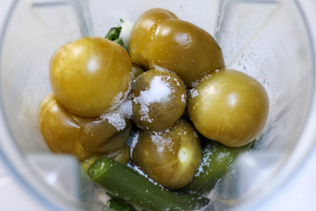 Tomatillos, serrano peppers and salt in a blender cup with a white background