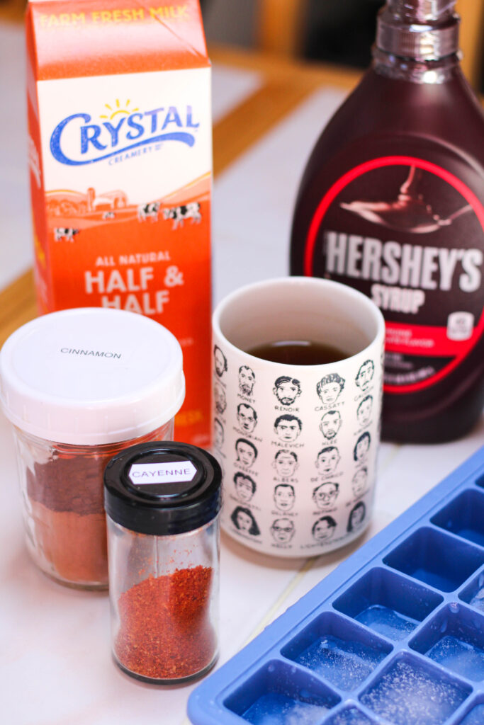 half and half, chocolate syrup, coffee, cinnamon and ice on a white table